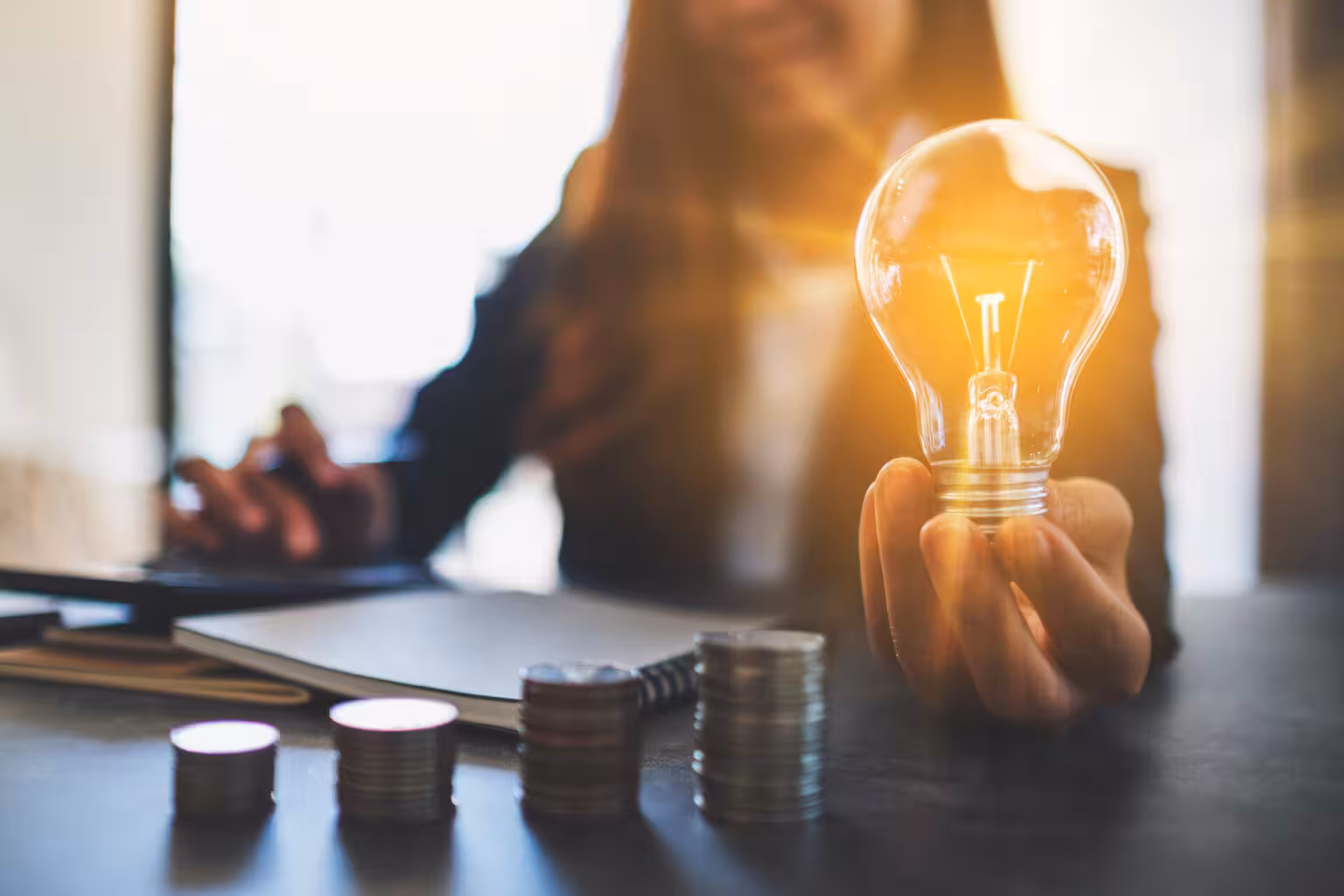 businesswoman-holding-a-lightbulb-with-coins-stack-2026-01-11-10-42-41-utc1536w.avif